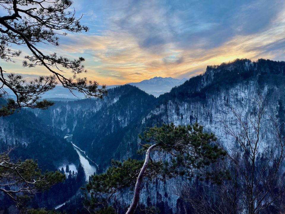 Photograph of mountains with a sunset behind and a river in the foreground